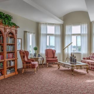 A cozy living room with armchairs, a coffee table, and a bookshelf against large windows.