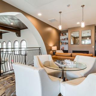 A modern living room with a stylish seating area featuring white armchairs around a glass table, complemented by elegant lighting and decorative wall design.