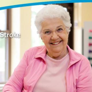 Elderly woman smiling indoors, wearing pink clothing.