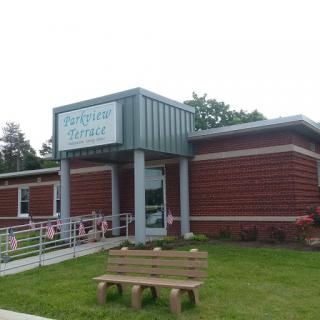 Exterior view of a modern brick building with a sign, featuring a seating area in front.