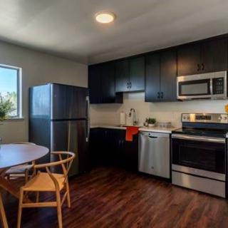 A modern kitchen with black cabinets, stainless steel appliances, and a wooden dining set.