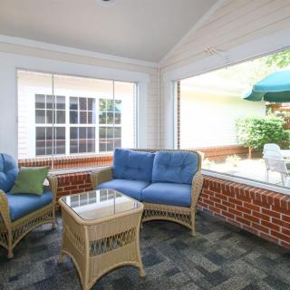 A cozy sunroom with wicker furniture and blue cushions, filled with natural light.