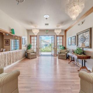 A bright and elegant lobby area with chandeliers, armchairs, and a wooden floor.