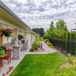 A beautifully landscaped backyard with a patio and outdoor furniture, showcasing a lush green lawn and a pathway lined with plants.