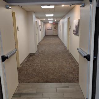 A view down a carpeted hallway with open doors and ceiling lights in an office environment.
