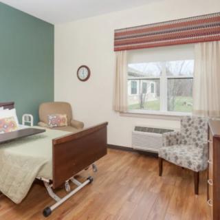 A clean and organized hospital room with a patient bed, chair, and window providing natural light.