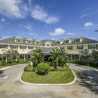 A charming hotel with a welcoming entrance surrounded by lush greenery under a clear blue sky.