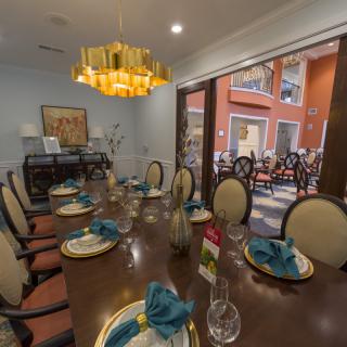 An elegantly decorated dining room with a large table set for a meal and a view of the outdoor patio through a glass door.