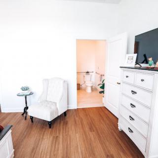 A cozy bedroom with a white chair, dresser, and wooden flooring.