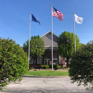 A building with three flags and surrounding greenery under a clear blue sky.