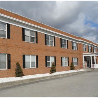 A brick building featuring multiple windows and a welcoming front entrance, set against a cloudy sky.