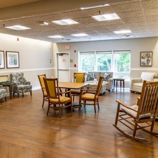 A spacious and well-lit common area featuring various seating options and tables with wooden flooring.