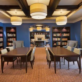 A cozy library reading room with bookshelves, tables, and chairs under warm lighting.