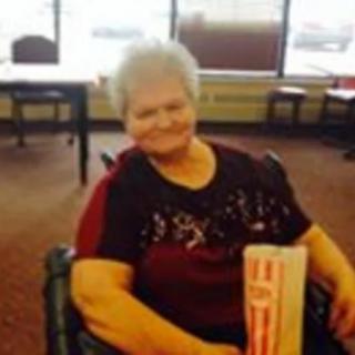 A smiling woman seated indoors holding an item.