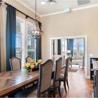 A spacious dining room with elegant decor, featuring a large wooden table, upholstered chairs, and a stylish chandelier.