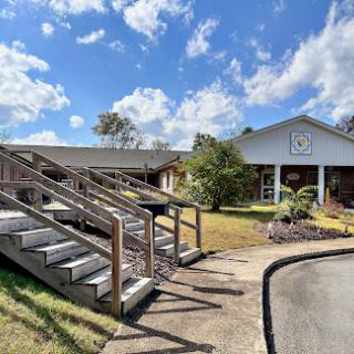 A welcoming building with accessible stairs, surrounded by lush greenery under a beautiful blue sky.
