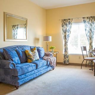 A cozy living room with a blue sofa and floral curtains, illuminated by natural light.
