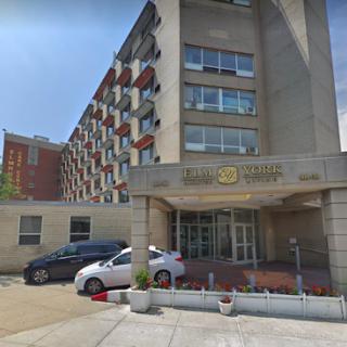 A modern hotel building with a welcoming entrance, surrounded by parked vehicles.