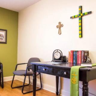 A small office space with a desk, chairs, and religious decor on the walls.