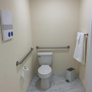 A clean and simple bathroom featuring a toilet with handrails, towel rack, and waste bin.