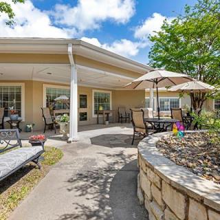 A sunny outdoor patio area with seating and umbrellas, surrounded by greenery and landscaping.