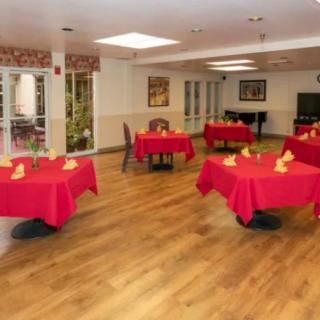 A dining area with red tablecloths on each table and a wooden floor, arranged in a cozy setting.