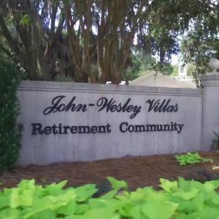 Entrance sign for John-Wesley Villas Retirement Community surrounded by greenery.