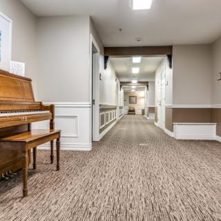 A well-lit hallway with a piano on the side, featuring carpeted flooring and elegant decor.