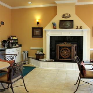 A cozy lounge area featuring a fireplace, coffee station, and seating with tables and chairs.