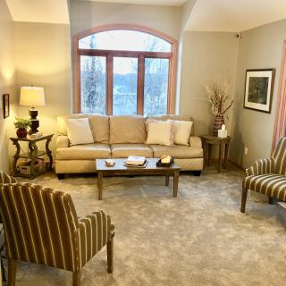A cozy living room with a beige sofa, striped chairs, and a large window.