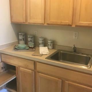 A kitchen with wooden cabinets, a countertop, and a sink, featuring storage jars.