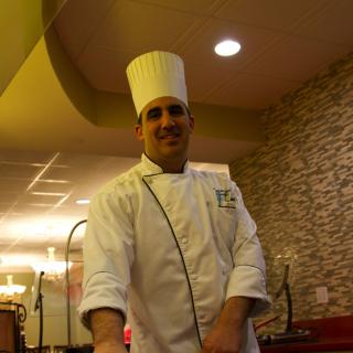 A chef in uniform standing inside a restaurant.