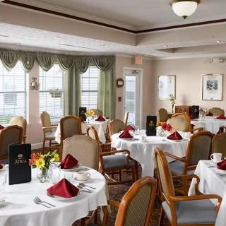 An elegant dining room with tables set for a meal, featuring white tablecloths and red napkins.
