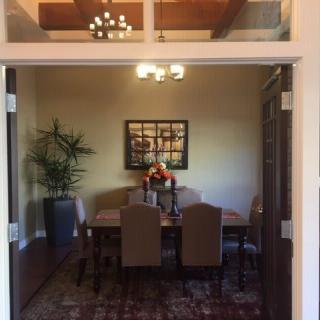 A cozy dining room with a wooden table, surrounded by upholstered chairs and illuminated by elegant ceiling lights.