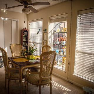 A cozy dining room bathed in sunlight, featuring a table with chairs and large windows with blinds.