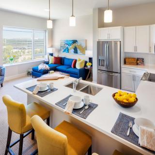 A modern open-concept kitchen and living room with bright lighting, featuring an island counter and stainless steel appliances.
