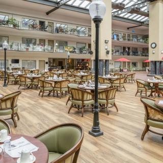 A spacious indoor dining area with multiple tables and chairs, featuring a glass canopy roof and decorative lighting.