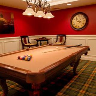 A cozy recreation room featuring a billiards table, red walls, and elegant lighting.