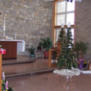 The interior of a church decorated for Christmas, featuring an altar and small Christmas trees.