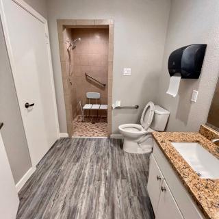 A modern bathroom with an accessible shower, featuring a sink, toilet, and paper towel dispenser.