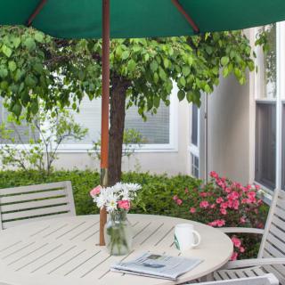 A serene patio setup with a round table and chairs under a green umbrella, adorned with a vase of flowers.