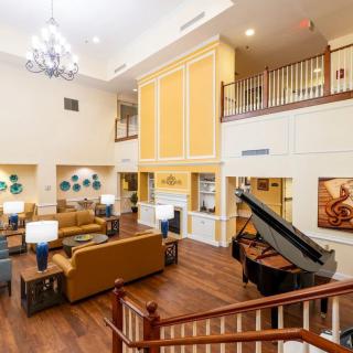 A spacious and elegantly designed lounge area featuring a grand piano, comfortable seating, and a chandelier.
