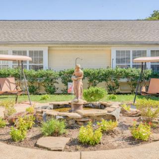 A picturesque courtyard featuring a central fountain with a sculpture, surrounded by swing benches and lush landscaping.