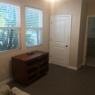 A simple room with a wooden cabinet, windows with blinds, and a doorway leading to another area.