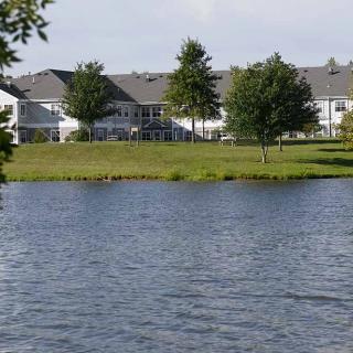 A serene lakeside view with houses and green trees in the background.