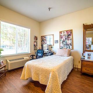 A cozy bedroom with a single bed, decorated with photographs and featuring a desk chair by the window.