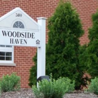 Sign for Woodside Haven in front of a brick building with greenery.