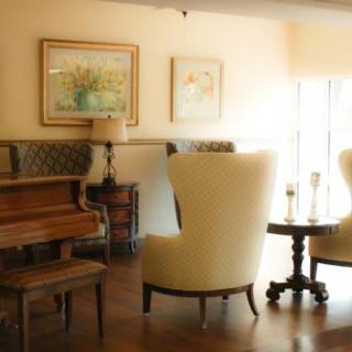 A cozy living room with a piano, elegant chairs, and framed artwork on the walls.