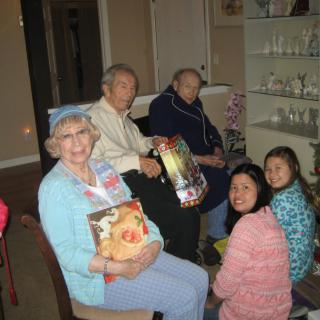 A multi-generational family gathering in a cozy indoor setting, with members exchanging gifts.