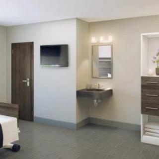 A modern hospital room with a bed, wall-mounted television, sink, and cabinetry.